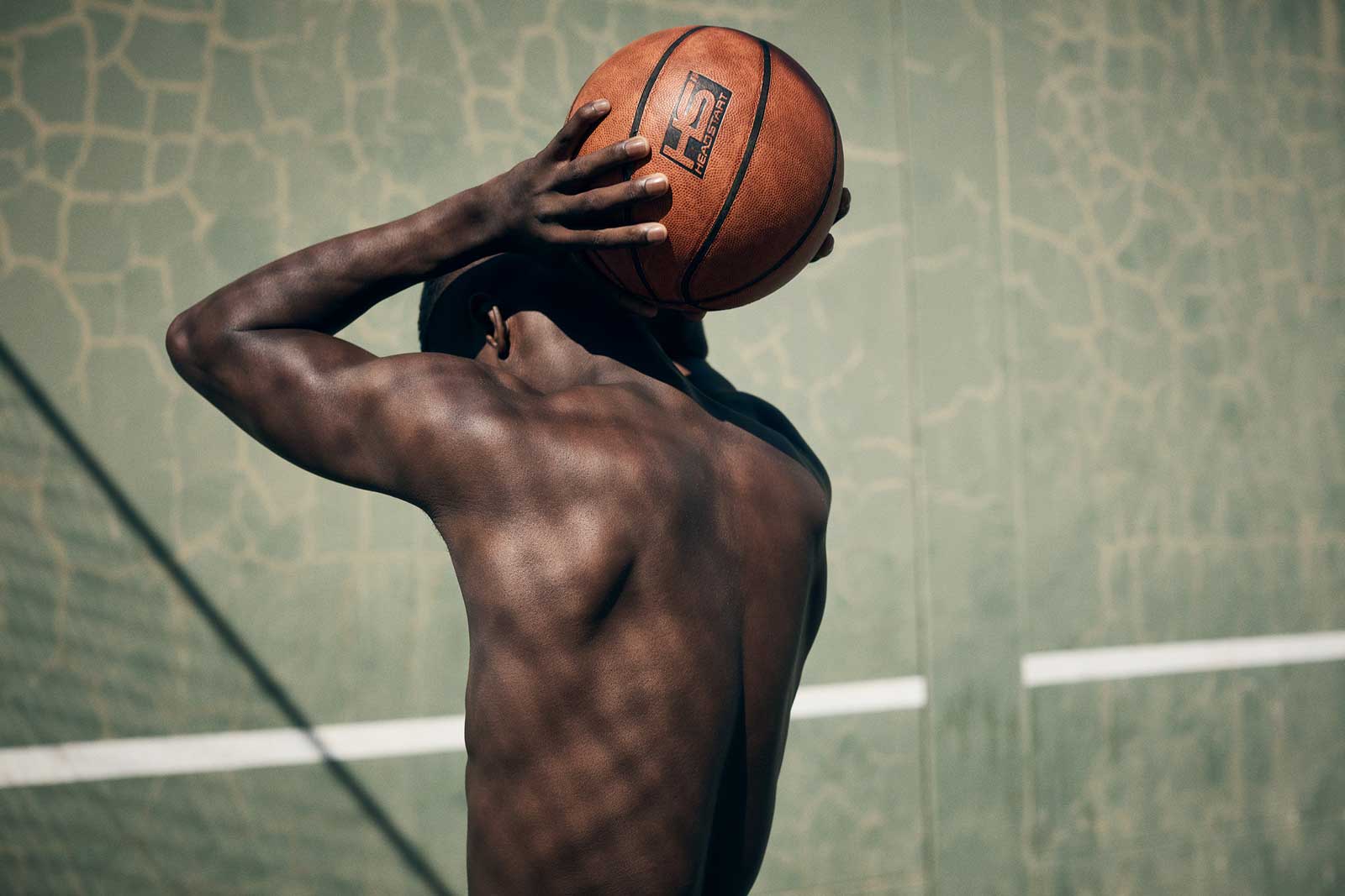 basketball player facing away holding a basketball to his head