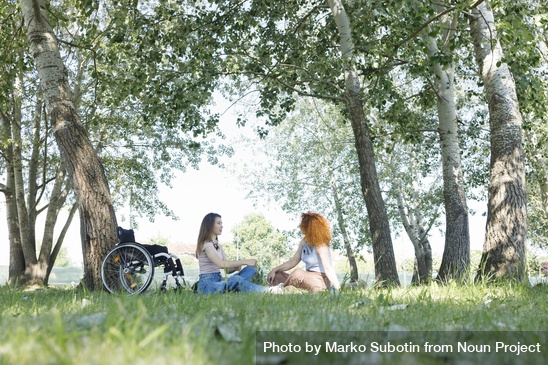 Two women chatting in a park with a wheel chair beside them